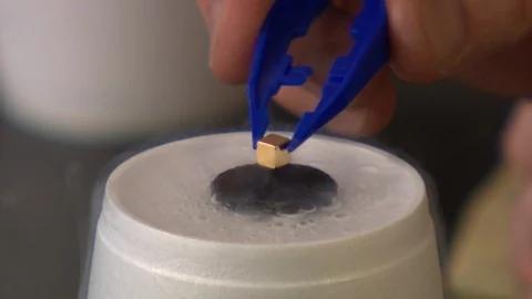 Small magnet levitating above a superconductor cooled by liquid nitrogen Stock Footage 99055916