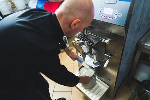 Small manufacturing man getting white vanilla ice cream out of ice cream maker Stock Photos