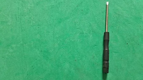 Small metal flathead screwdriver resting on a vibrant green surface Fotos de archivo