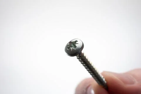 Small metal threaded screw held by Caucasian male hand between fingers. Close Fotos de archivo