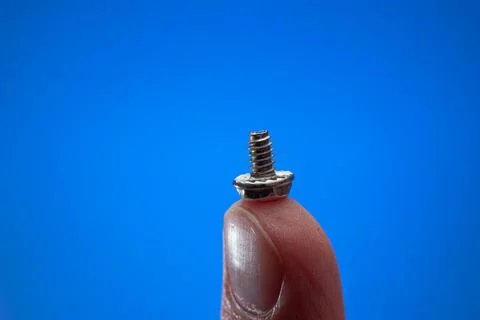 Small metal threaded screw held by Caucasian male hand between fingers. Close 스톡 사진