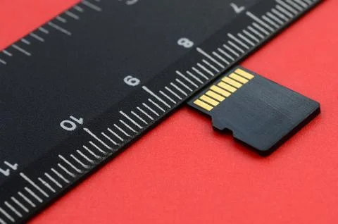 Small micro SD memory card lie on a red background next to a black ruler. A s Stock Photos