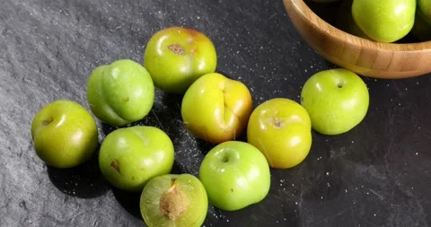 Small mini green fresh juicy plum fruit in wooden bowl on black slate stone b Stock Footage 205583448