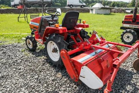 A small mini red tractor stands on a farm yard on green grass and waits for work Stock Photos
