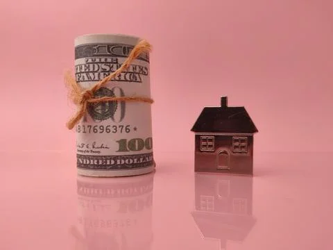 A small model house next to a roll of United States currency Stock Photos