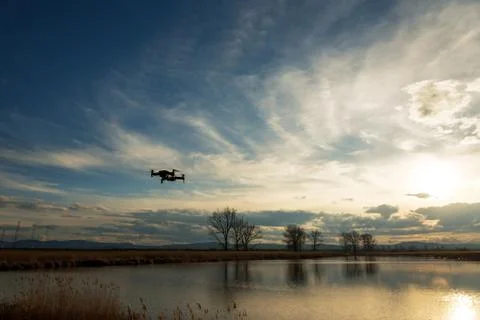 Small modern drone hovering taking picture of sunset. Stock Photos