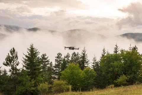 Small modern drone hovering taking picture of sunrise in mountain. Stock Photos