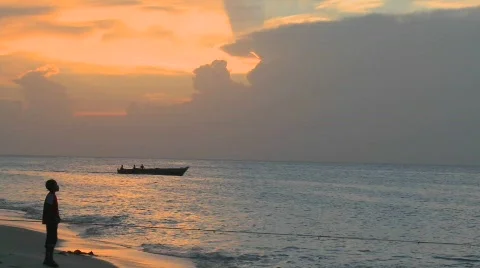 A small motorboat heads out at sunset as people walk on the beach at Stone Town, Stock Footage