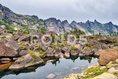 Small mountain lake in glacial moraine from large boulders Stock Photos