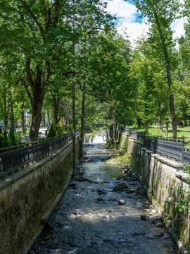 Small mountain river flowing through green park embankment in resort town Фото