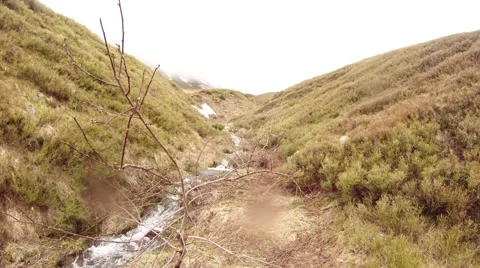 Small Mountain Stream Between Slopes of Hills in Highlands in Light Haze Stock Footage 63961459