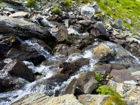 A small mountain stream flows through the stones on the slope Stock Photos