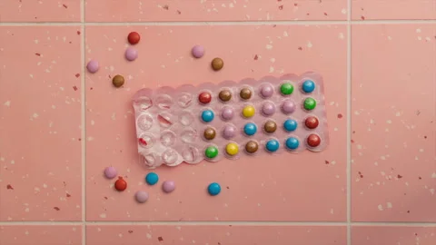 Small multi-colored round candies on a pink background in time-lapse Stock Footage 256183560