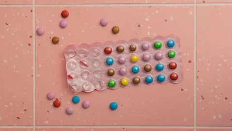 Small multi-colored round candies on a pink background in dynamic time-lapse Stock Footage 256183625