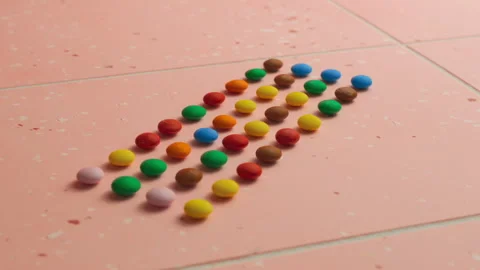 Small multi-colored round candies on a pink background Stock Footage 256183674