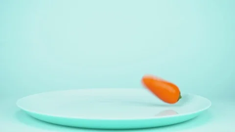 Small multicolored bell peppers fall on the blue dish on a blue background Stock Footage 121634440