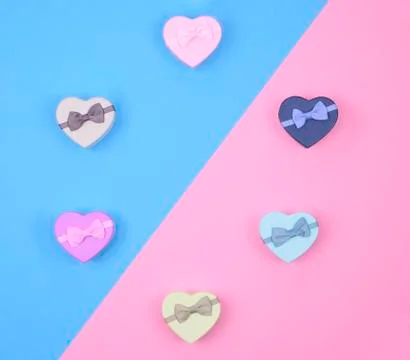 Small multicolored gift boxes hearts on blue and pink background, top view, c Stock Photos