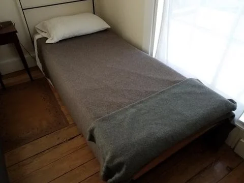 Small narrow old bed with grey and black blankets Stock Photos