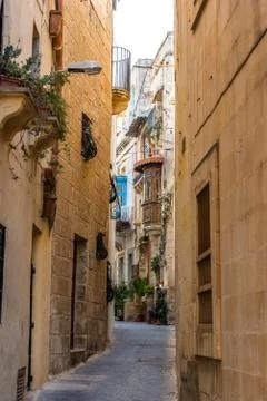 Small narrow street on Malta with ancient buildings in the light of sunset Stock Photos