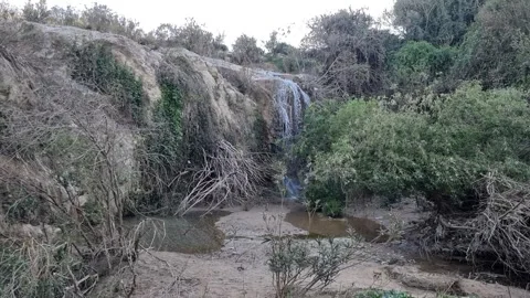 Small natural waterfall cascading down a rocky cliff surrounded by wild Stockbeeldmateriaal 339062727