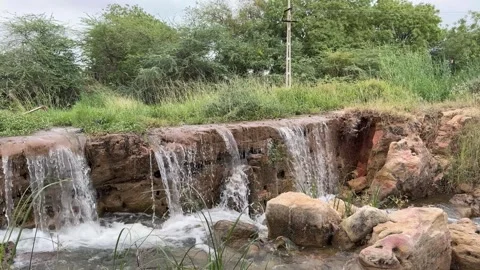 Small Natural Waterfall Cascading over Rocks in a Green Rural Stream Stock Footage 332779345