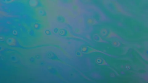 Small objects looking like semen moving in a rainbow colored liquid. Color Video stock 128579525