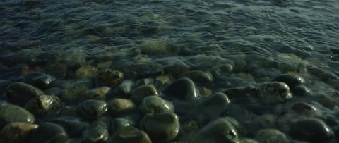 Small ocean waves crash over smooth stones Stockbeeldmateriaal 135477723