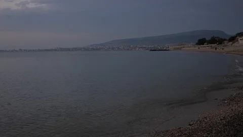 Small ocean waves roll on rocky beach against distant hill Stock Footage 124023701