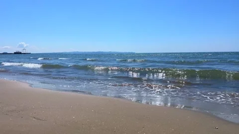 Small Ocean Waves Rolling onto Sandy Shore Under Clear Blue Sky Stock Footage 310232868