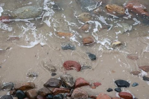Small ocean waves washing over smooth stones on a rocky beach. Shoreline de.. Foto stock