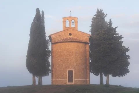 Small, old stone chapel stands enveloped in morning fog, surrounded by tall Foto stock