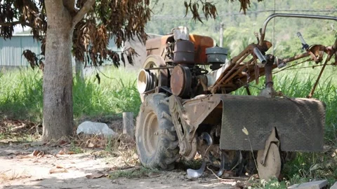 A small old tractor sits in a rural field beside a tree, with grass and open lan Stock Footage 342335907