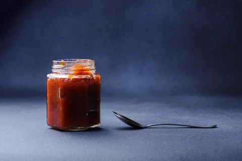 Small open jar with apple jam against dark blue background Stock-Fotos