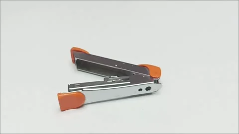 Small orange and silver metal stapler on white background Stock Footage 338140603