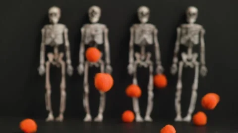 Small orange balls are falling against the background of four skeletons in blur. Stock Footage 160697987
