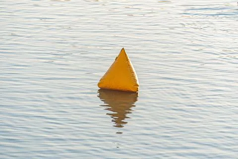 Small orange buoy floating on tranquil water, contrasting with backdrop of .. Stock Photos