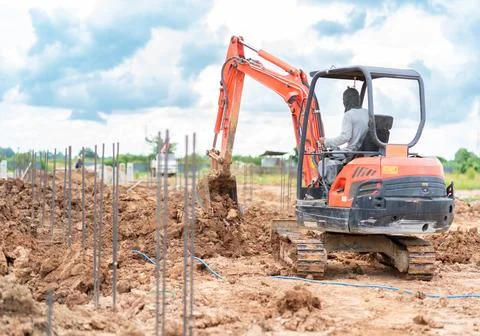 Small orange excavator digging soil at an outdoor construction site with fo.. 스톡 사진