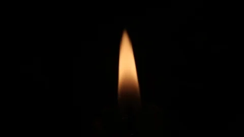 A small orange flame of a candle burns in darkness. Solid black background Vidéo 122456101