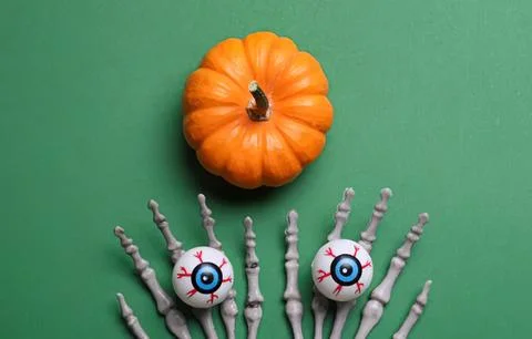 Small orange pumpkin with spooky eyeball decorations on green background Stock Photos