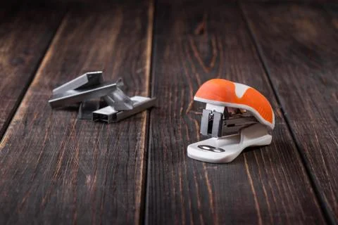 A small orange stapler and staples on a wooden background. Close-up. Copy spa Stock Photos