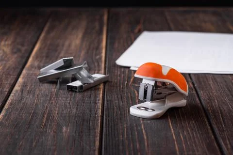 A small orange stapler and staples on a wooden background. Close-up. Copy spa Stock Photos