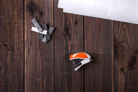 A small orange stapler and staples on a wooden background. Close-up. Copy spa Stock Photos