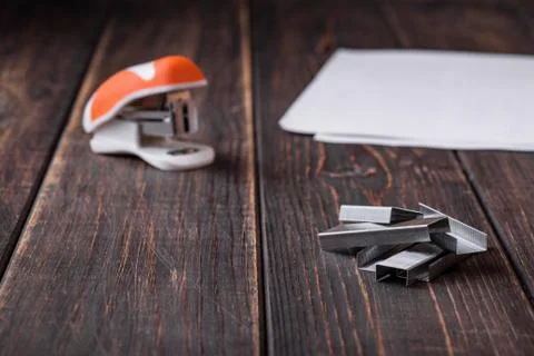 A small orange stapler and staples on a wooden background. Close-up. Copy spa Stock Photos