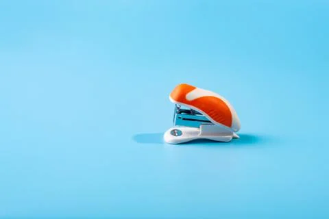 A small orange stapler in blue background. Close-up. Copy space. Space for te Stock Photos