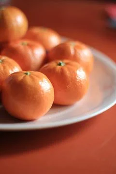 Small oranges are placed in a white plate on the orange table. Stock Photos