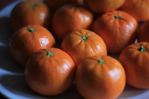 Small oranges are placed in a white plate on the orange table. Stock Photos