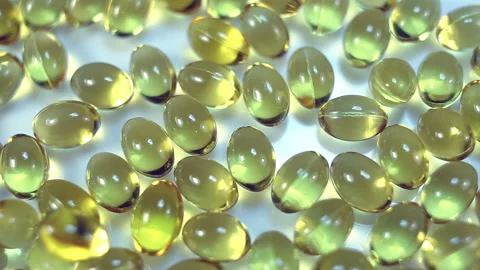 Small oval transparent gel capsules have a yellow oily liquid inside. On a blue Stock Footage 144952302