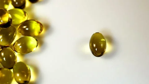 A small oval transparent yellow capsule falls on a white background. Real-time, Stock Footage 145108906