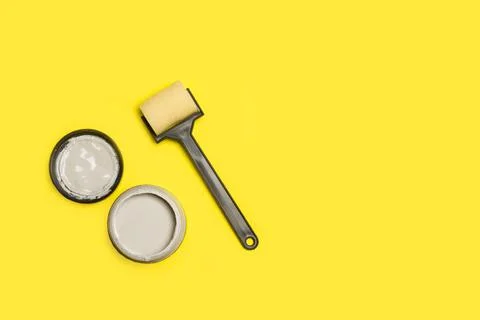 A small paint roller and a paint pot on a yellow background with copy space Stock Photos