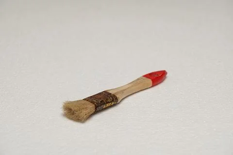 Small paintbrush with red tip on white surface Stock Photos